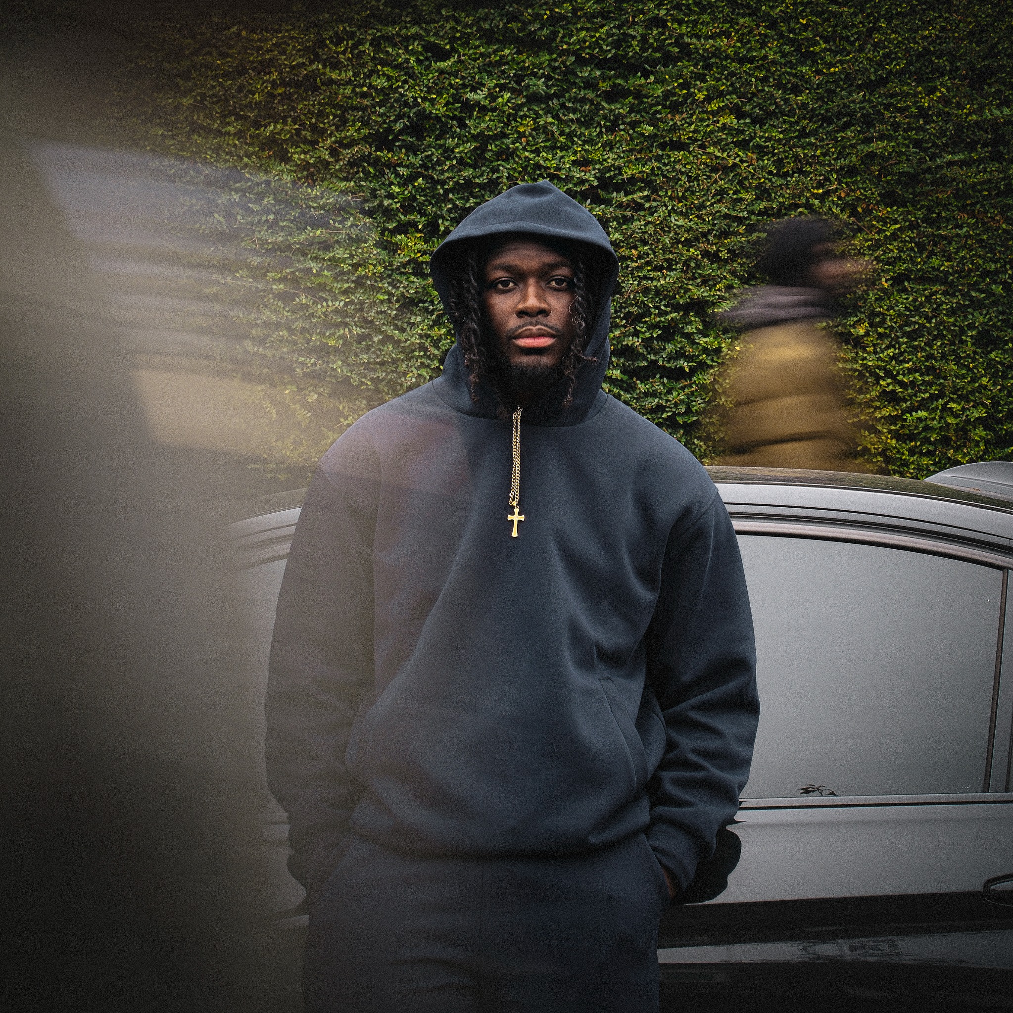 Elikem standing in a dark hood beside a car